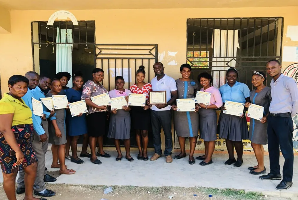 House of Hope counselors and training graduates holding certificates outside a school in Haiti